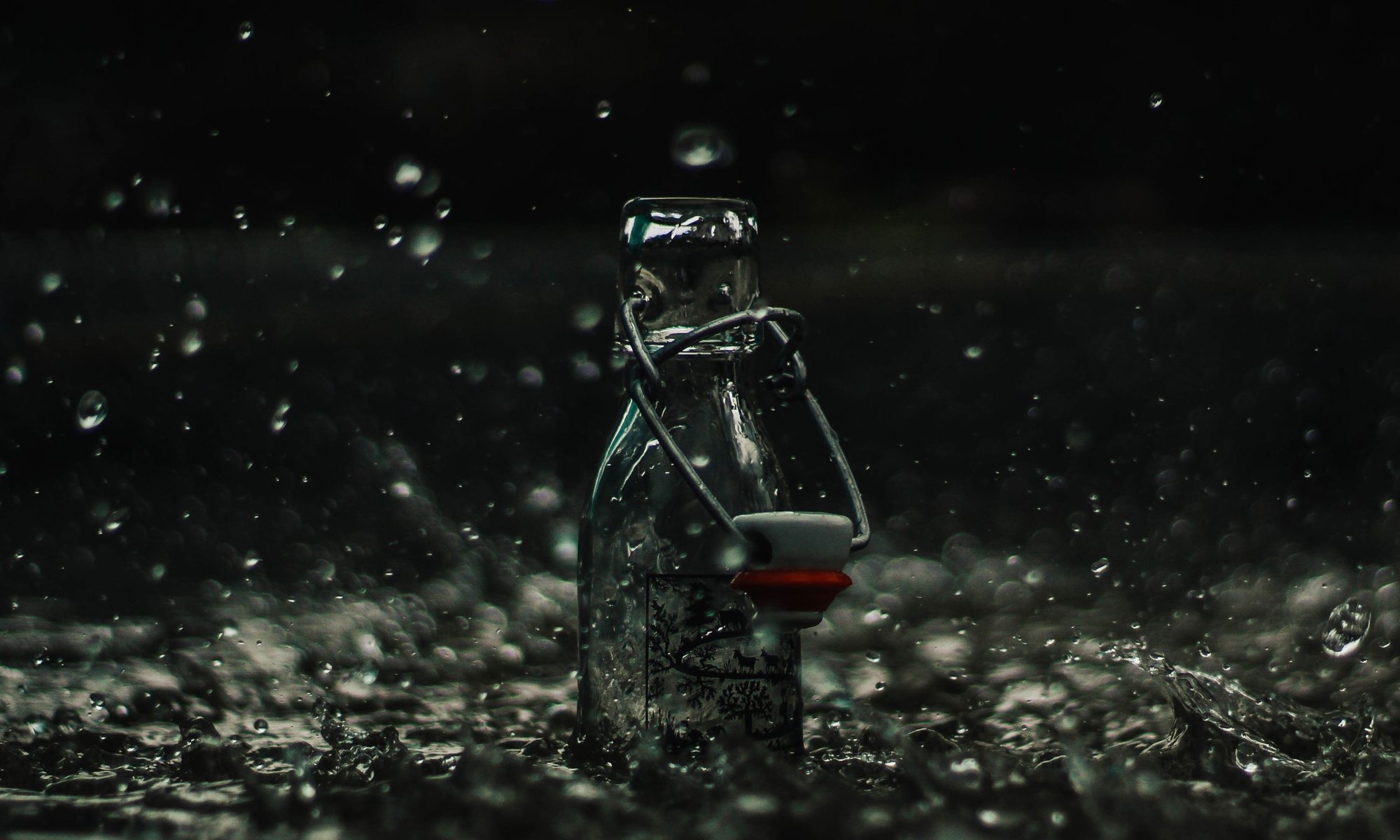 Glass bottle in rain with splashing water.